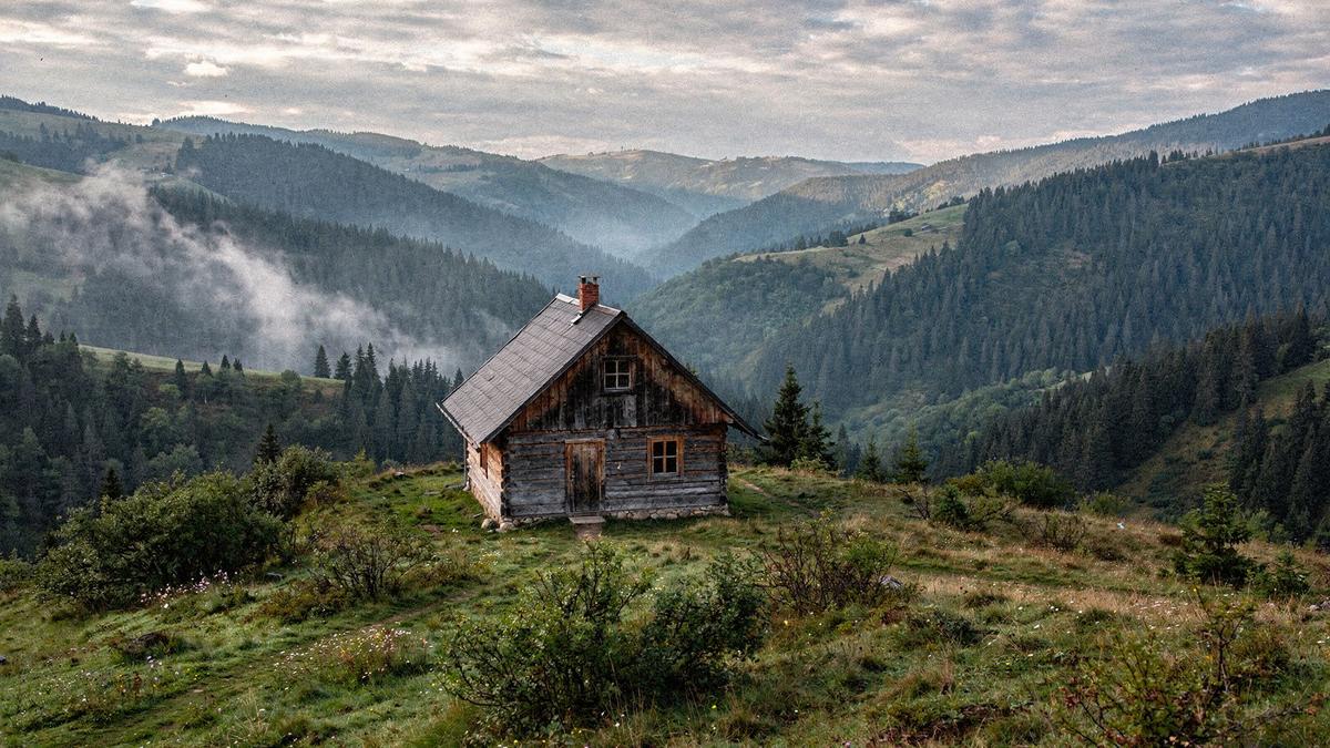 Timber guest house on a green Carpathian ridge above a valley in morning mist